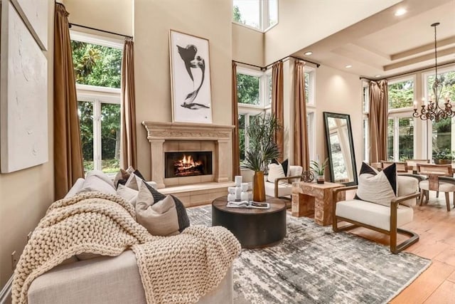 living area with a warm lit fireplace, a chandelier, recessed lighting, wood finished floors, and a towering ceiling