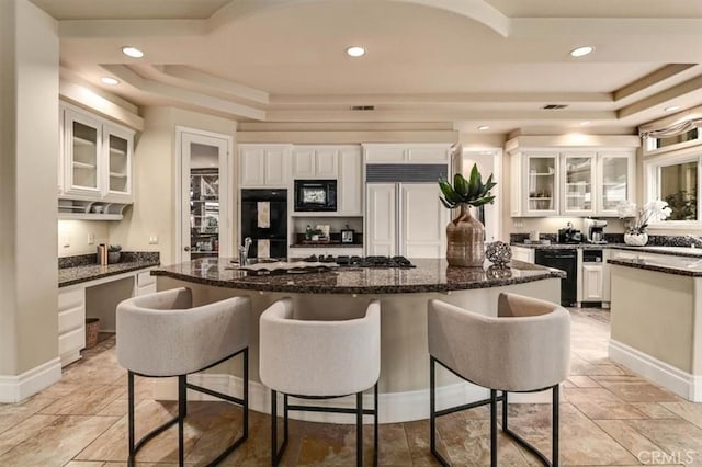 kitchen with a raised ceiling, white cabinets, a breakfast bar area, and black appliances