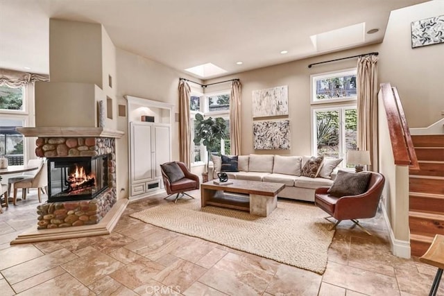 living area featuring a skylight, a stone fireplace, and plenty of natural light
