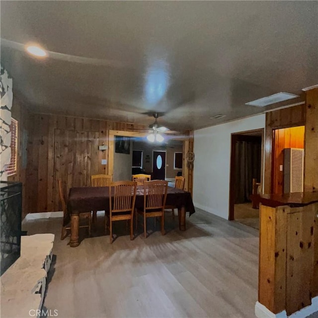 dining room featuring wood walls, wood finished floors, and a ceiling fan