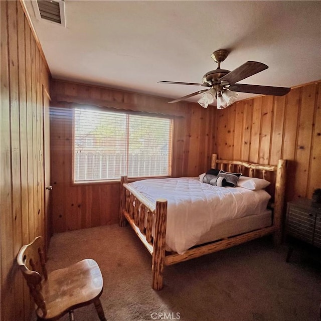 carpeted bedroom with wood walls, visible vents, and a ceiling fan