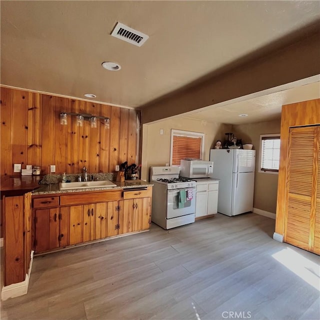 kitchen with visible vents, light wood-style flooring, brown cabinetry, a sink, and white appliances