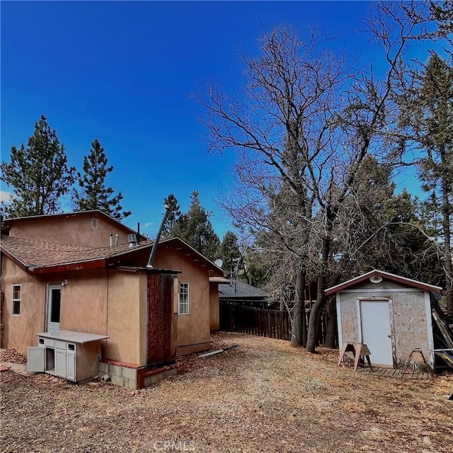 view of side of home with stucco siding, fence, an outdoor structure, and a shed