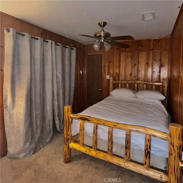 carpeted bedroom with ceiling fan, wooden walls, and visible vents