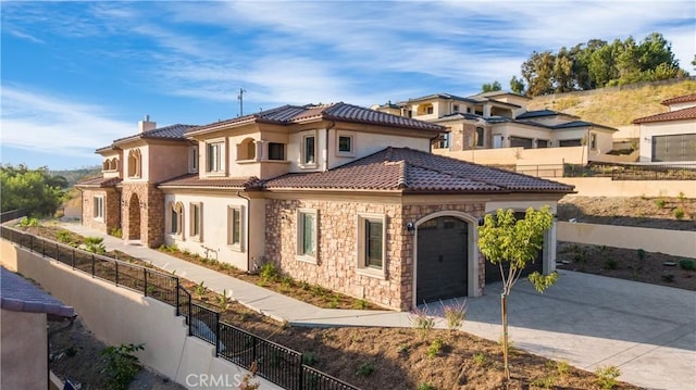 mediterranean / spanish house featuring stone siding, a tiled roof, fence, and driveway