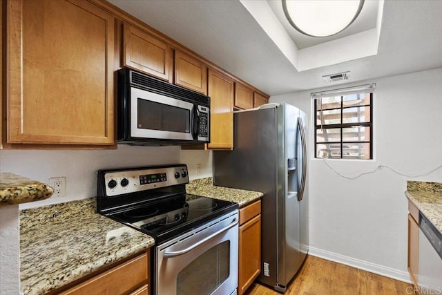 kitchen featuring a tray ceiling, light hardwood / wood-style flooring, stainless steel appliances, and light stone countertops