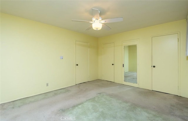 unfurnished bedroom with light carpet, ceiling fan, and multiple closets