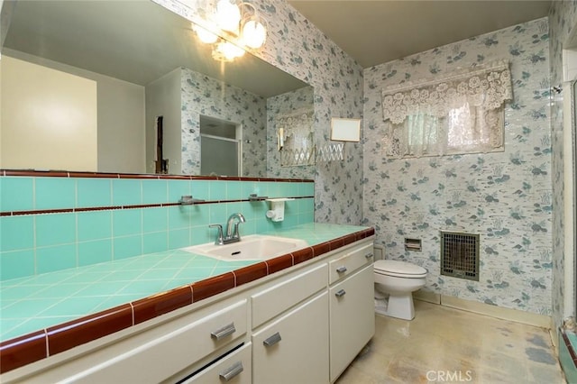 bathroom with toilet, a shower with shower door, vanity, and tasteful backsplash