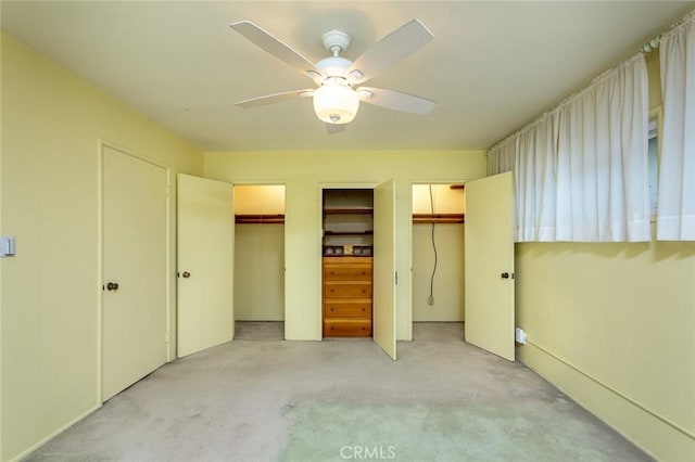 unfurnished bedroom with light carpet, ceiling fan, and multiple closets