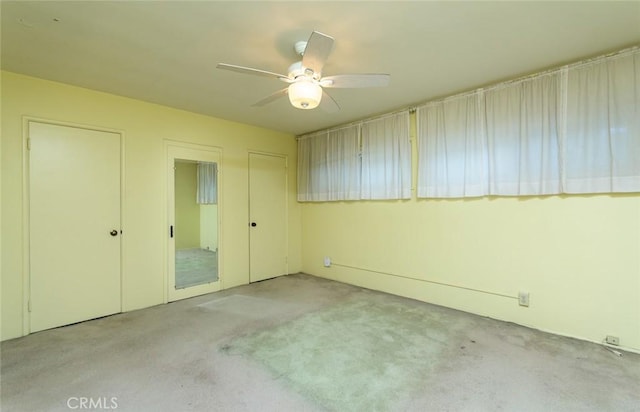 unfurnished bedroom with ceiling fan, two closets, and light colored carpet