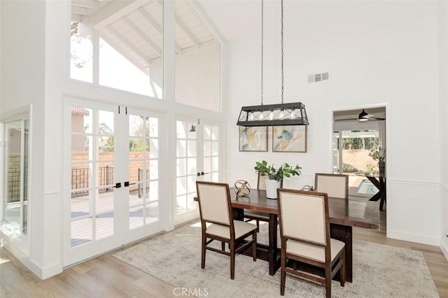 dining space featuring french doors, visible vents, light wood-style flooring, and a towering ceiling