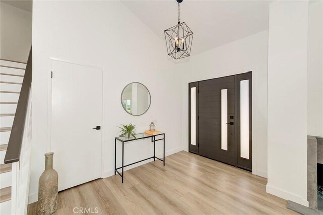 entrance foyer featuring light wood finished floors, stairway, high vaulted ceiling, and an inviting chandelier