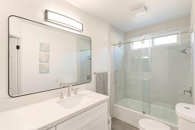 full bath with toilet, shower / bath combination with glass door, tile patterned flooring, and vanity