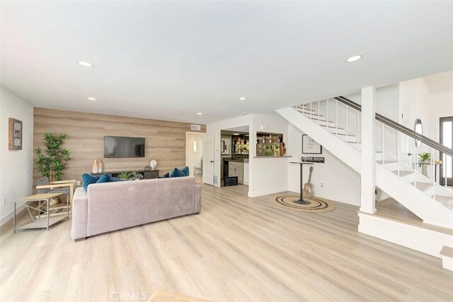 living area with light wood-style flooring, an accent wall, stairway, wood walls, and recessed lighting