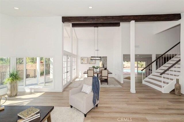 living area featuring light wood-style flooring, beam ceiling, stairway, and a high ceiling