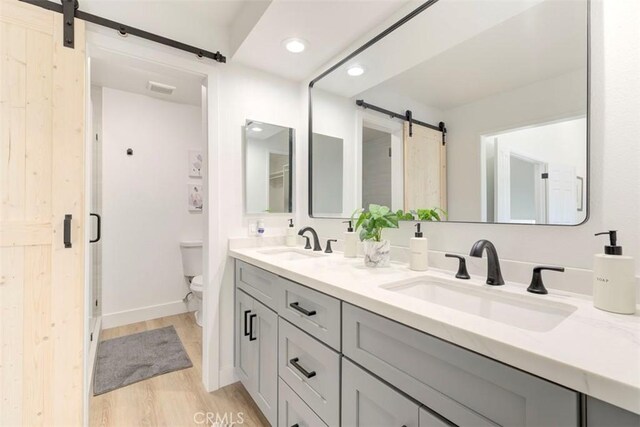 bathroom featuring double vanity, a sink, toilet, and wood finished floors