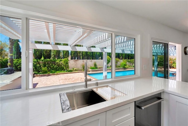 kitchen featuring a sink, light countertops, white cabinetry, and dishwashing machine