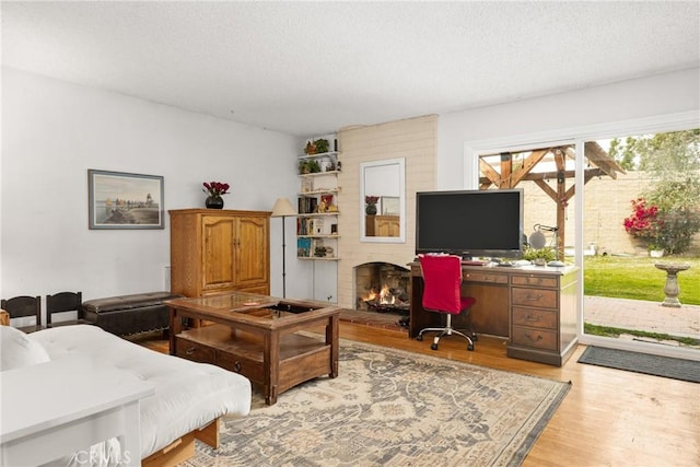 home office featuring a brick fireplace, light hardwood / wood-style flooring, and a textured ceiling