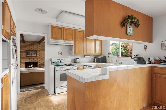 kitchen with tile counters, kitchen peninsula, a fireplace, sink, and white gas stove