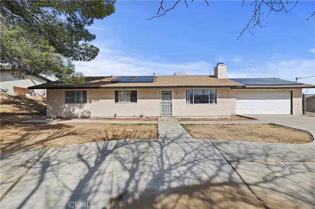 ranch-style home featuring stucco siding, driveway, roof mounted solar panels, an attached garage, and a chimney