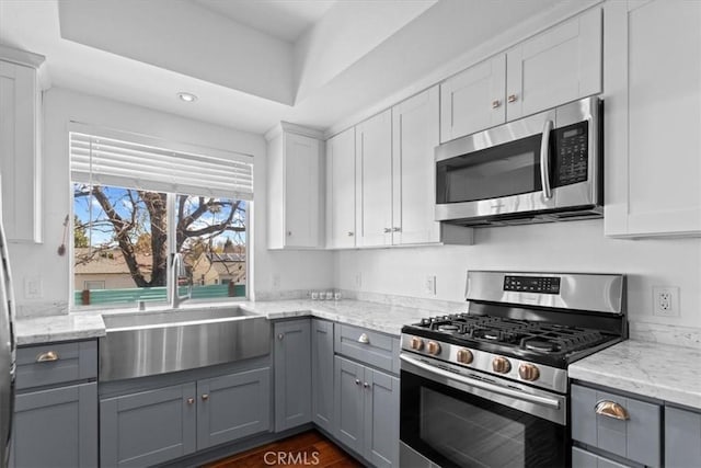 kitchen with appliances with stainless steel finishes, light stone counters, gray cabinetry, white cabinetry, and a sink