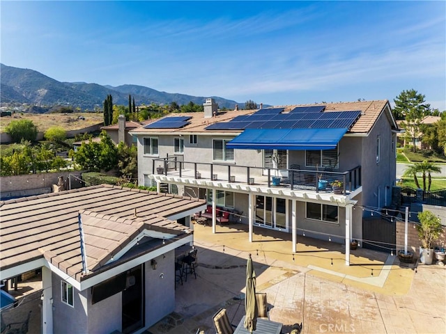 rear view of property featuring a balcony, roof mounted solar panels, a mountain view, and a patio