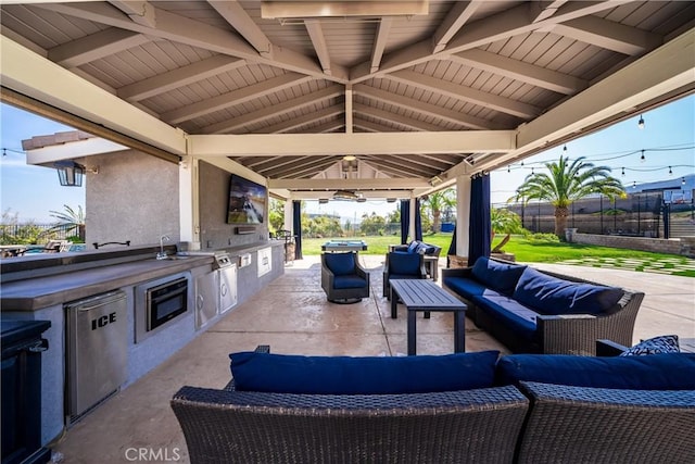 view of patio with outdoor lounge area, a sink, fence, a gazebo, and exterior kitchen