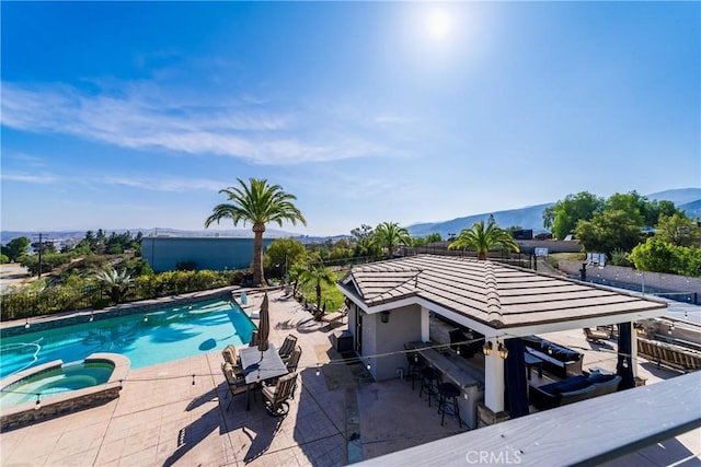 view of pool featuring a pool with connected hot tub, a bar, a patio, and a mountain view