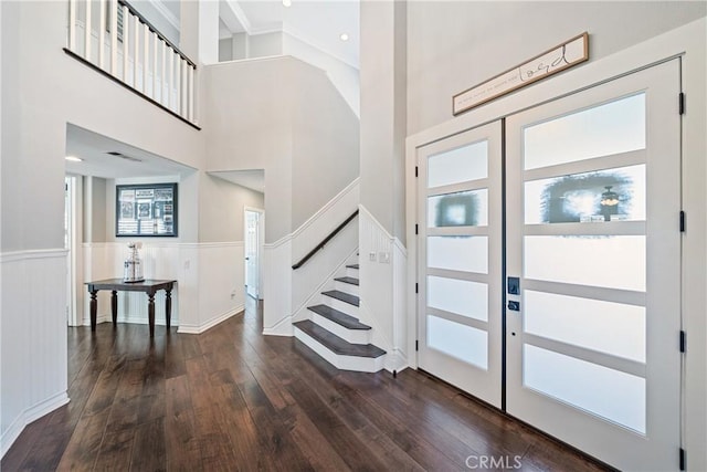 foyer featuring dark wood-style flooring, a wainscoted wall, stairway, and a high ceiling