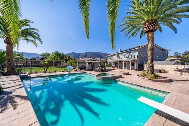 view of swimming pool with a patio, a pool with connected hot tub, a mountain view, fence, and a diving board