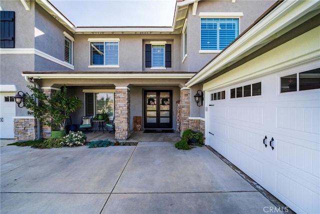 doorway to property with a garage, stone siding, driveway, and stucco siding