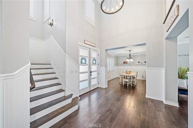 entryway with a wainscoted wall, stairs, ornamental molding, dark wood-style floors, and an inviting chandelier