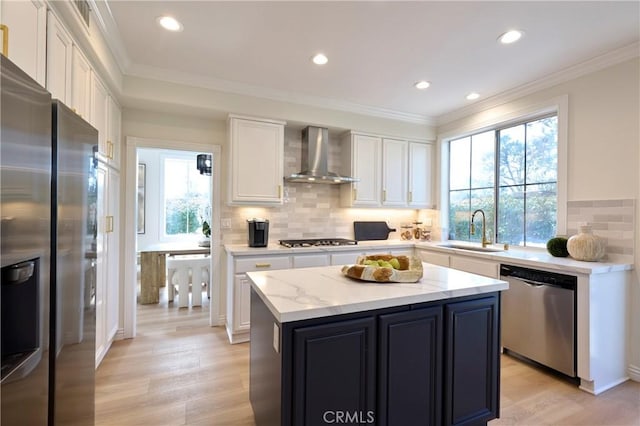 kitchen with white cabinets, a center island, stainless steel appliances, wall chimney range hood, and a sink