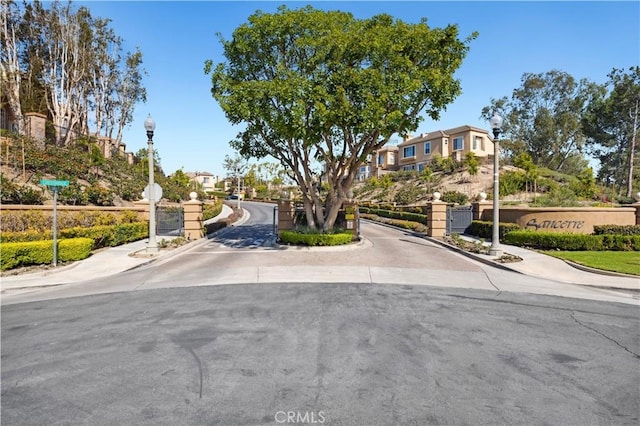 view of street featuring street lights, a gate, sidewalks, a gated entry, and curbs