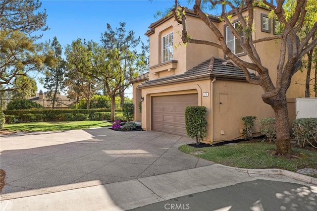 view of side of property featuring concrete driveway, a tile roof, fence, and stucco siding