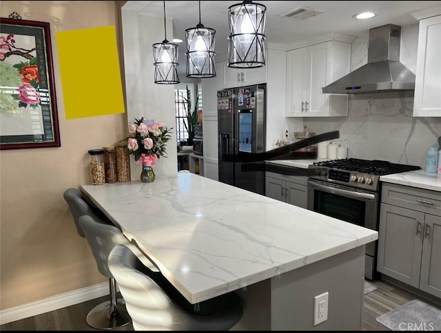 kitchen featuring hanging light fixtures, wall chimney range hood, appliances with stainless steel finishes, and a kitchen breakfast bar