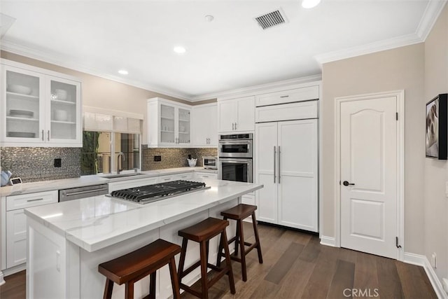 kitchen with white cabinets, a kitchen island, glass insert cabinets, stainless steel appliances, and a sink