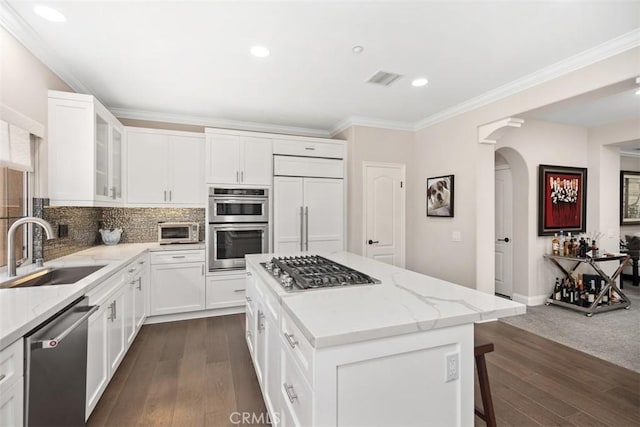 kitchen featuring stainless steel appliances, a kitchen island, a sink, white cabinets, and glass insert cabinets