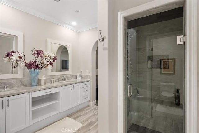 full bathroom with crown molding, double vanity, a sink, a shower stall, and wood finished floors