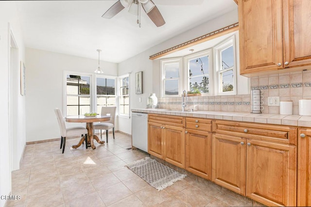 kitchen with tile countertops, white dishwasher, a sink, backsplash, and decorative light fixtures