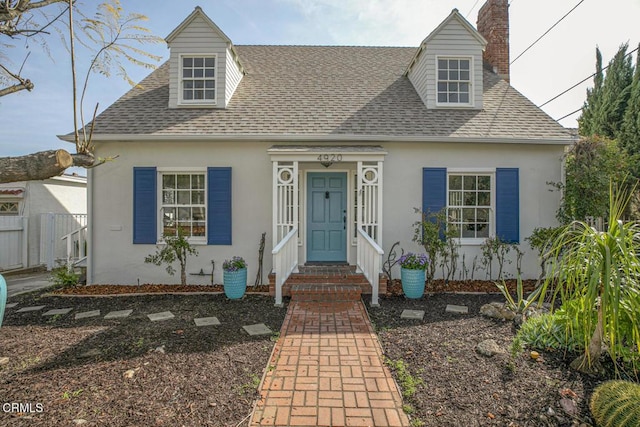 cape cod home with entry steps, a shingled roof, fence, and stucco siding