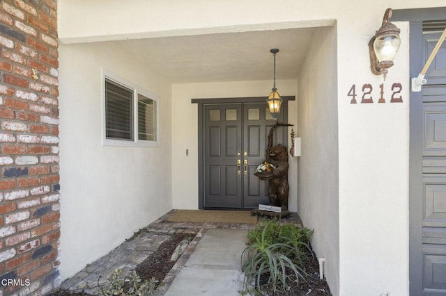 entrance to property with stucco siding, covered porch, and brick siding