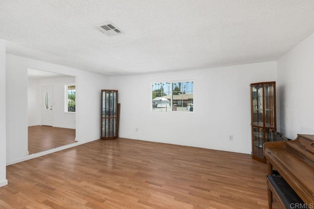 empty room with a textured ceiling and light hardwood / wood-style flooring