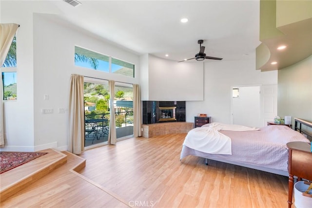 bedroom featuring a glass covered fireplace, wood finished floors, recessed lighting, baseboards, and access to exterior