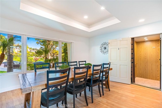 dining room featuring recessed lighting, light wood-style flooring, baseboards, and a tray ceiling