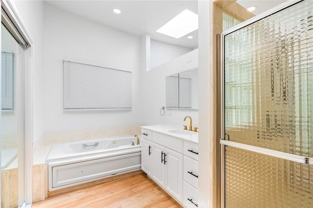 bathroom featuring a garden tub, recessed lighting, a skylight, wood finished floors, and vanity