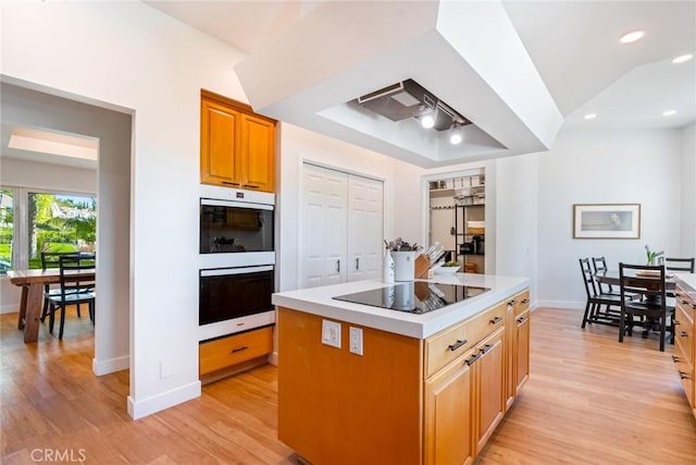 kitchen with light wood-type flooring, a tray ceiling, black electric stovetop, and white double oven