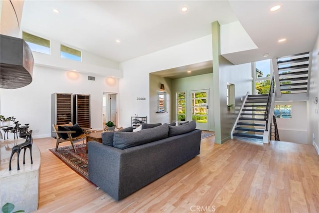 living area featuring stairway, baseboards, light wood finished floors, a high ceiling, and recessed lighting