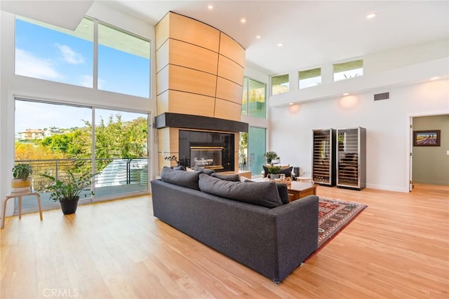 living room featuring baseboards, visible vents, light wood finished floors, a high ceiling, and a tile fireplace