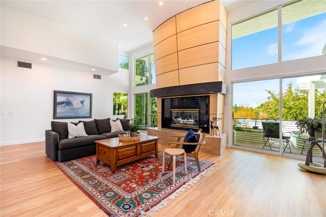 living room featuring a high ceiling, a fireplace, visible vents, and light wood-type flooring